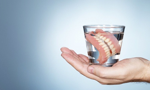 hand holding glass of water with full dentures 