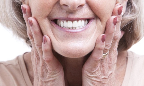 close up of older woman smiling and holding her face 