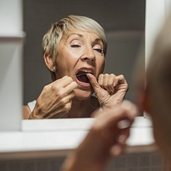 mature woman flossing in mirror