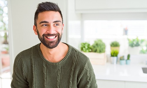 person smiling and sitting in a kitchen with a sweater on