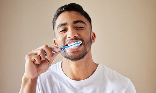 Man smiling while brushing his teeth