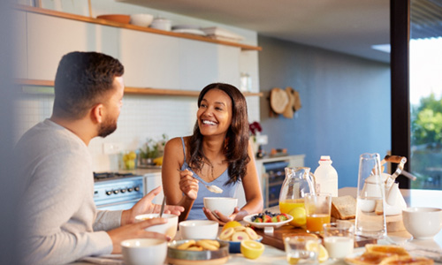 Couple smiling at each other while eating in kitchen