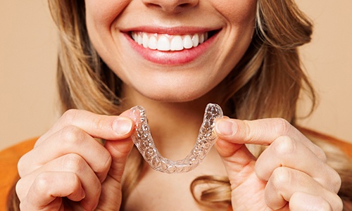 Patient smiling while holding clear aligner