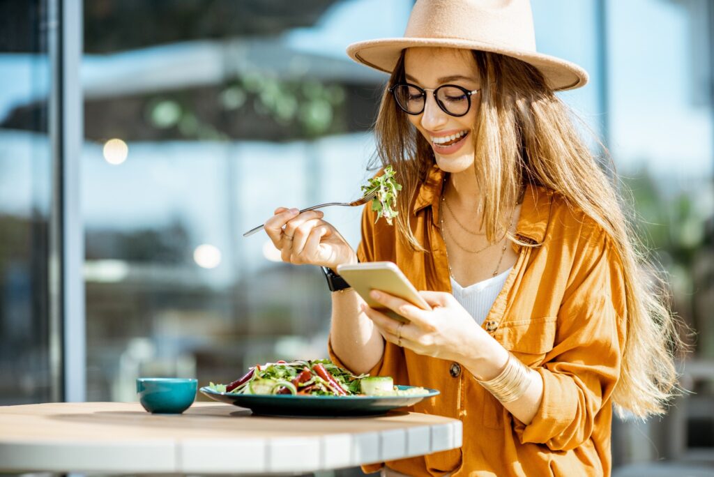 Woman smiling at phone while eating lunch outside